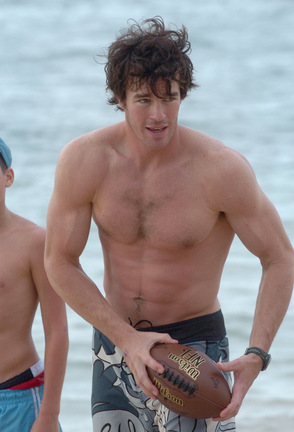 Ryan Sutter oberkörperfrei mit Football am Strand