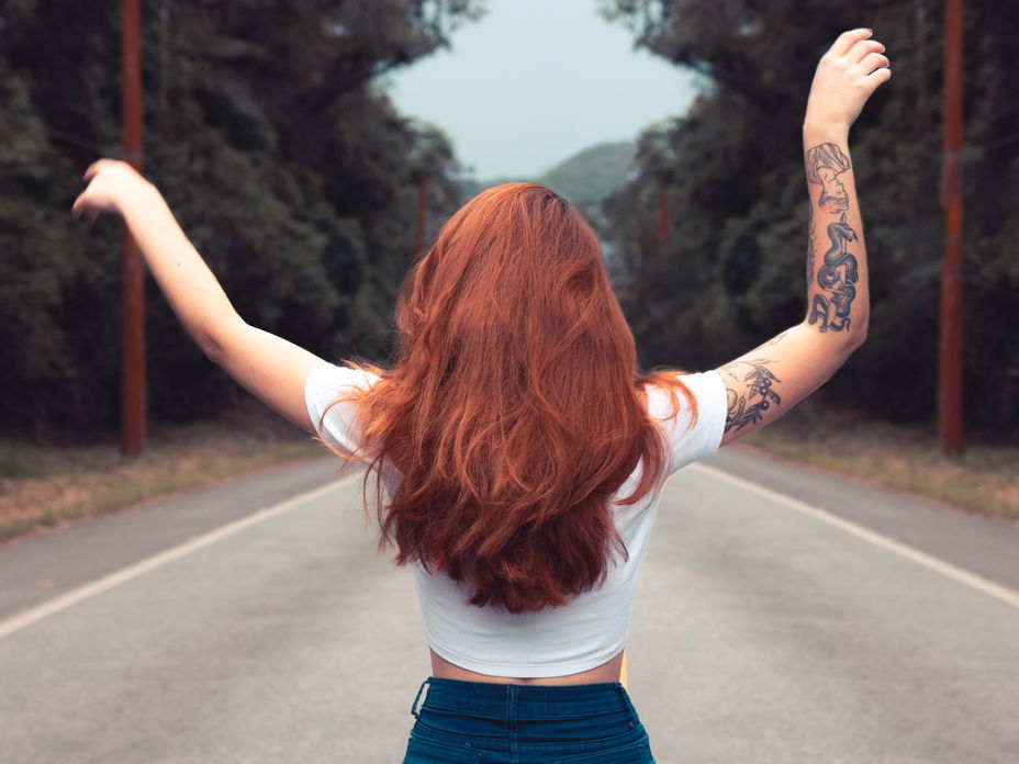 Rothaarige Frau auf einer Straße im Wald mit Tattoos am rechten Arm