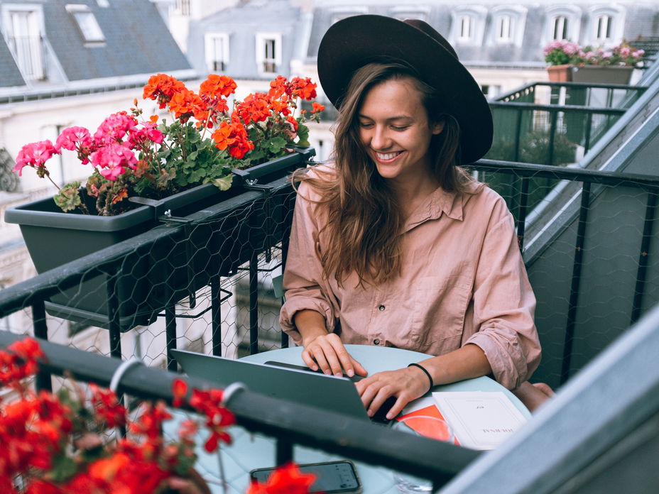 Junge Frau sitzt auf dem Balkon am Laptop