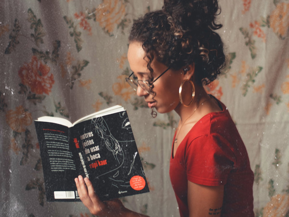 Mädchen mit Buch und Tasse in den Händen vor geblümter Wand