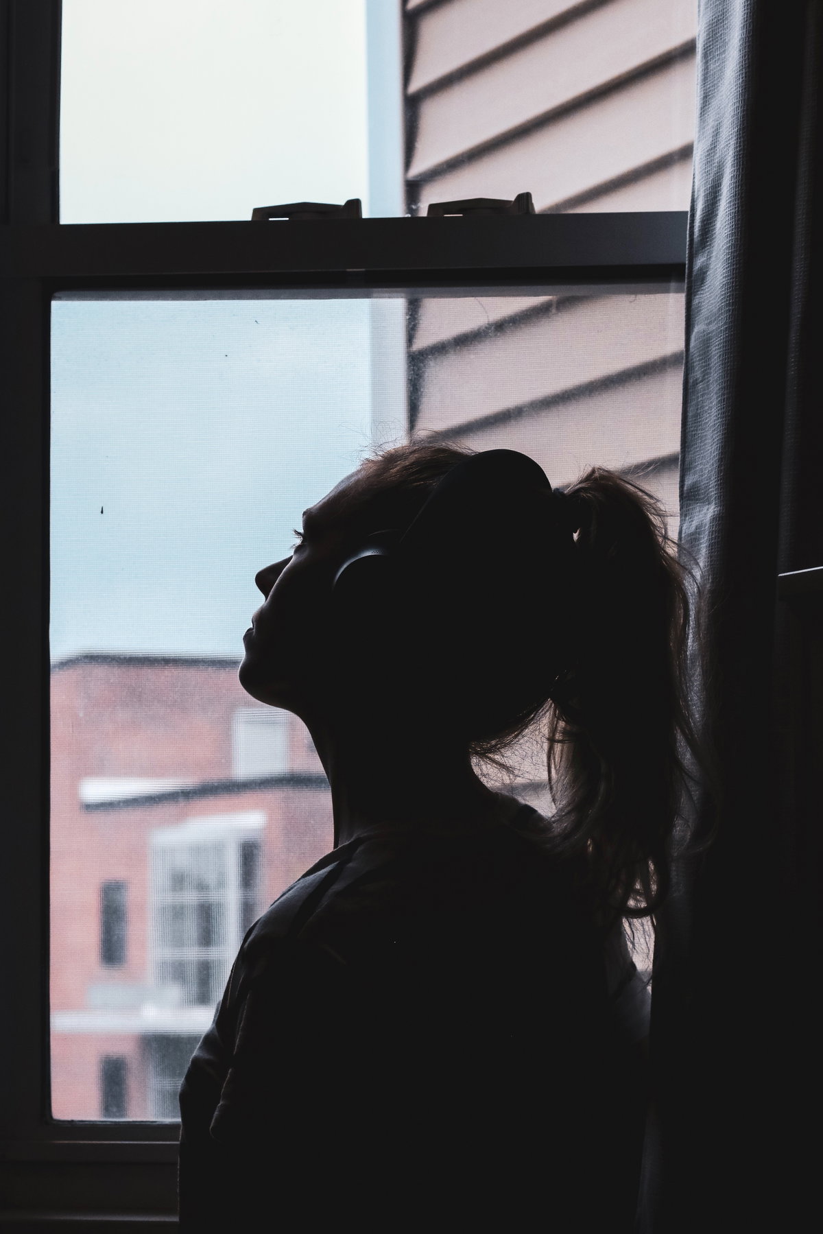 Frau am offenen Fenster mit Kopfhörern