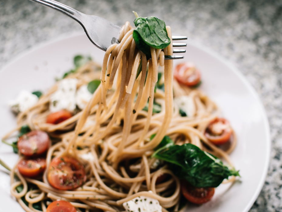 Weißer Teller mit Pasta, Tomaten und Spinat