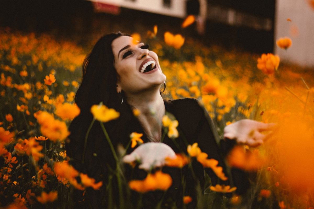 Frau sitzt in Blumen-Feld und lacht