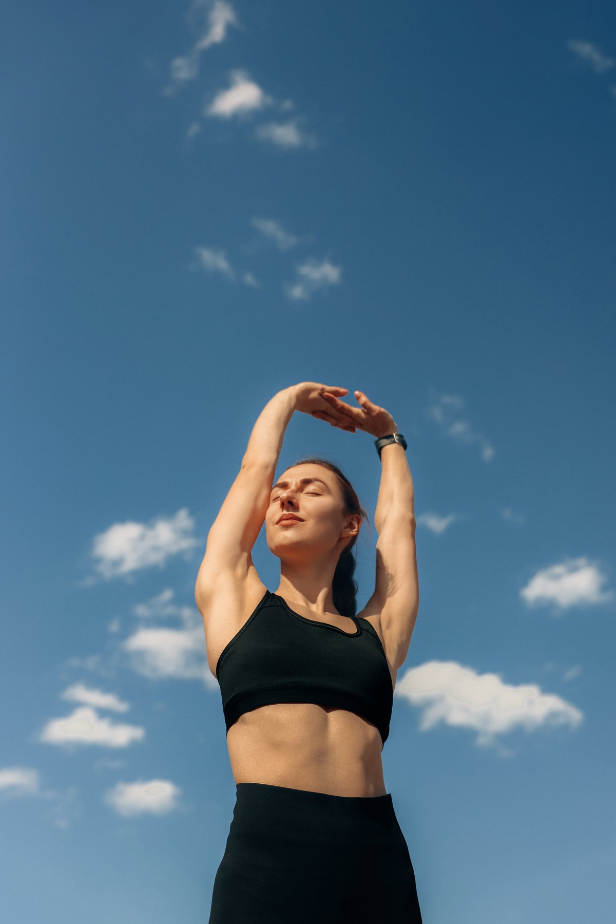 Frau mit Sport-Bh und Sporleggings streckt die Arme in den Himmel