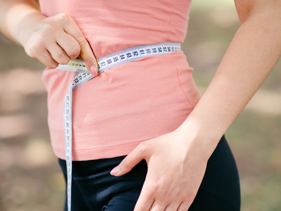 Frau hält Maßband an ihren Bauch