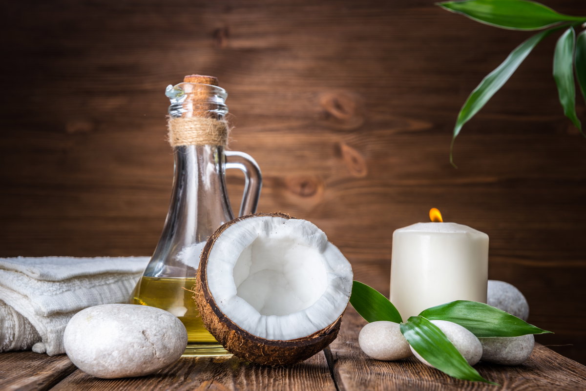 Kokosöl Haare: Ölflasche steht neben einer halben Kokosnuss und einer Kerze auf einem Tisch