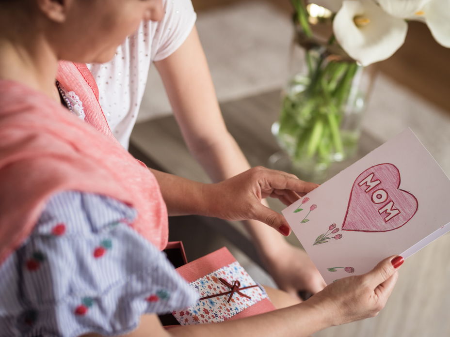 Muttertagssprüche: Frau hält eine Karte in der Hand auf der "Mom" steht