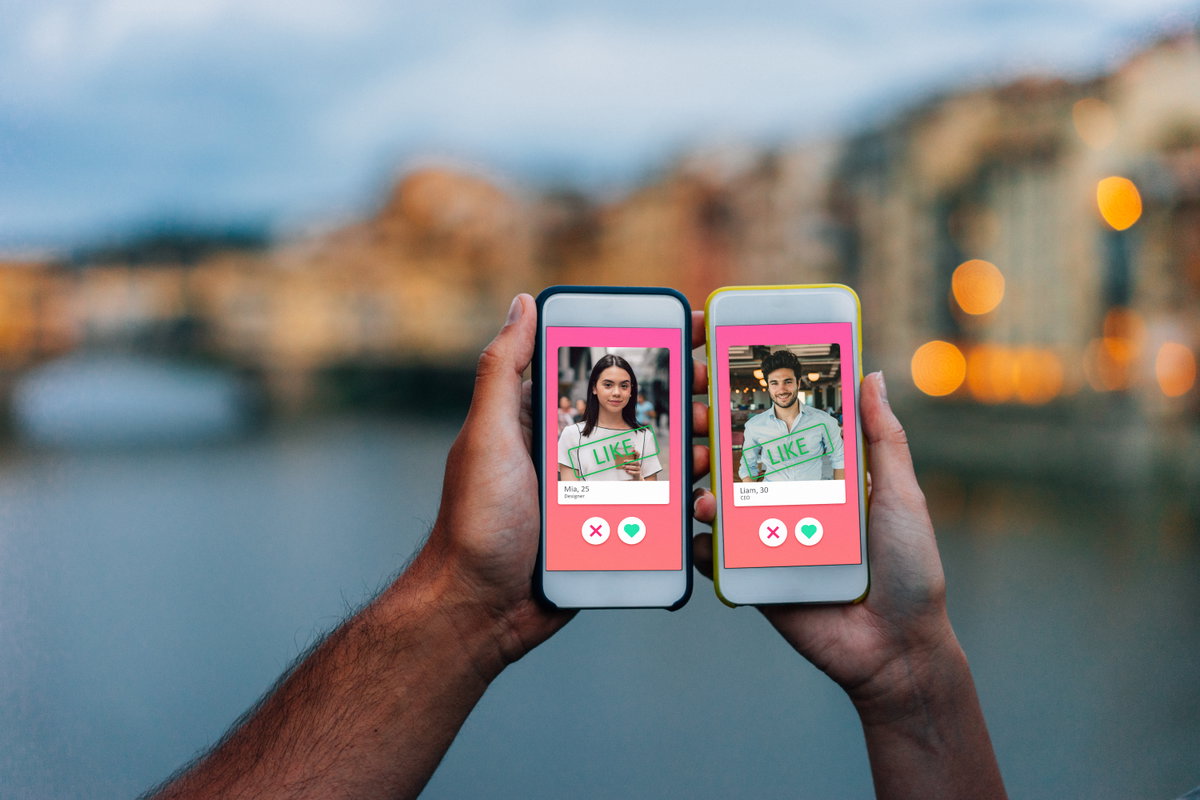 Hand von Mann und Frau mit Smartphone jeweils in der Hand, auf welchem Tinder geöffnet ist