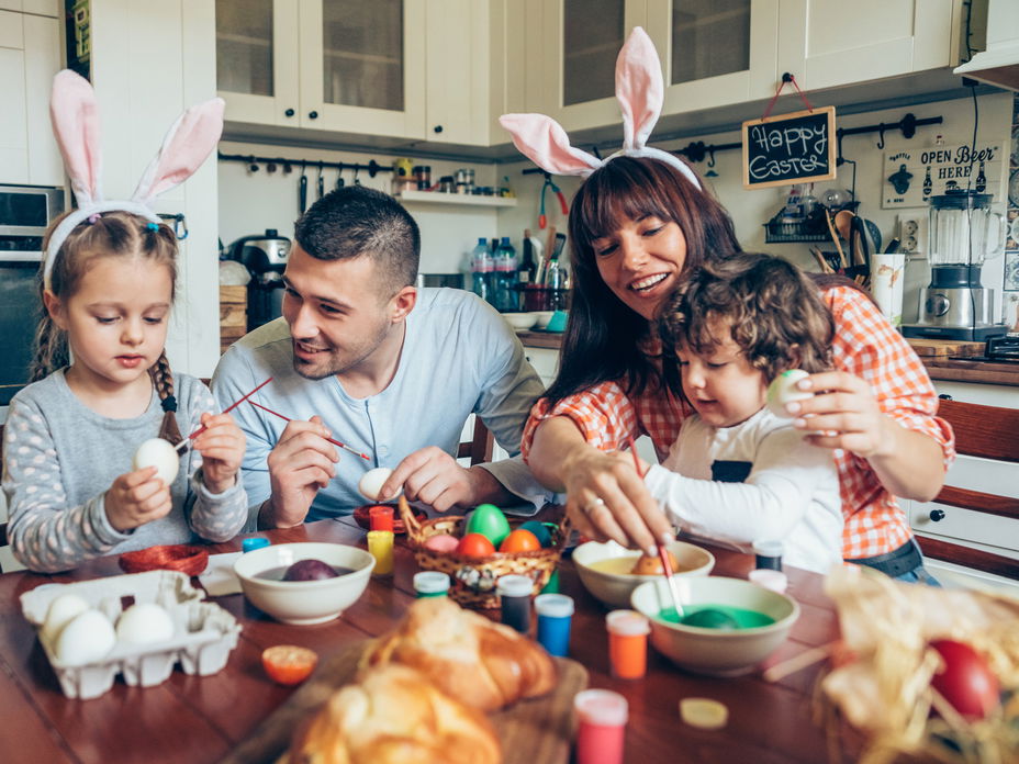 Warum feiern wir Ostern? Familie sitzt am Tisch und bemalt Ostereier