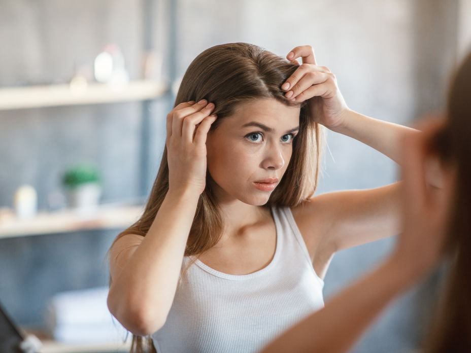 Wie schnell wachsen Haare? Frau steht vor Spiegel und schaut sich den Haaransatz an