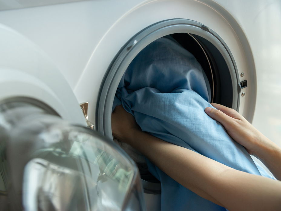 Bettwäsche waschen: Hände packen blaue Bettbezüge in eine Waschmaschine