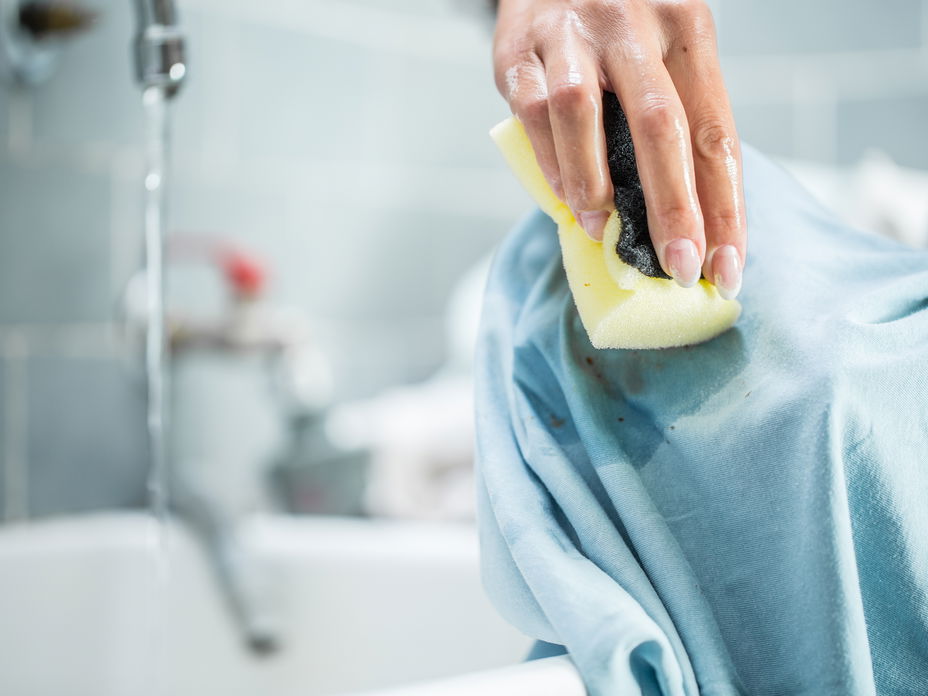 Fettflecken entfernen: Hand wäscht Fleck mit Schwamm aus Kleidungsstück