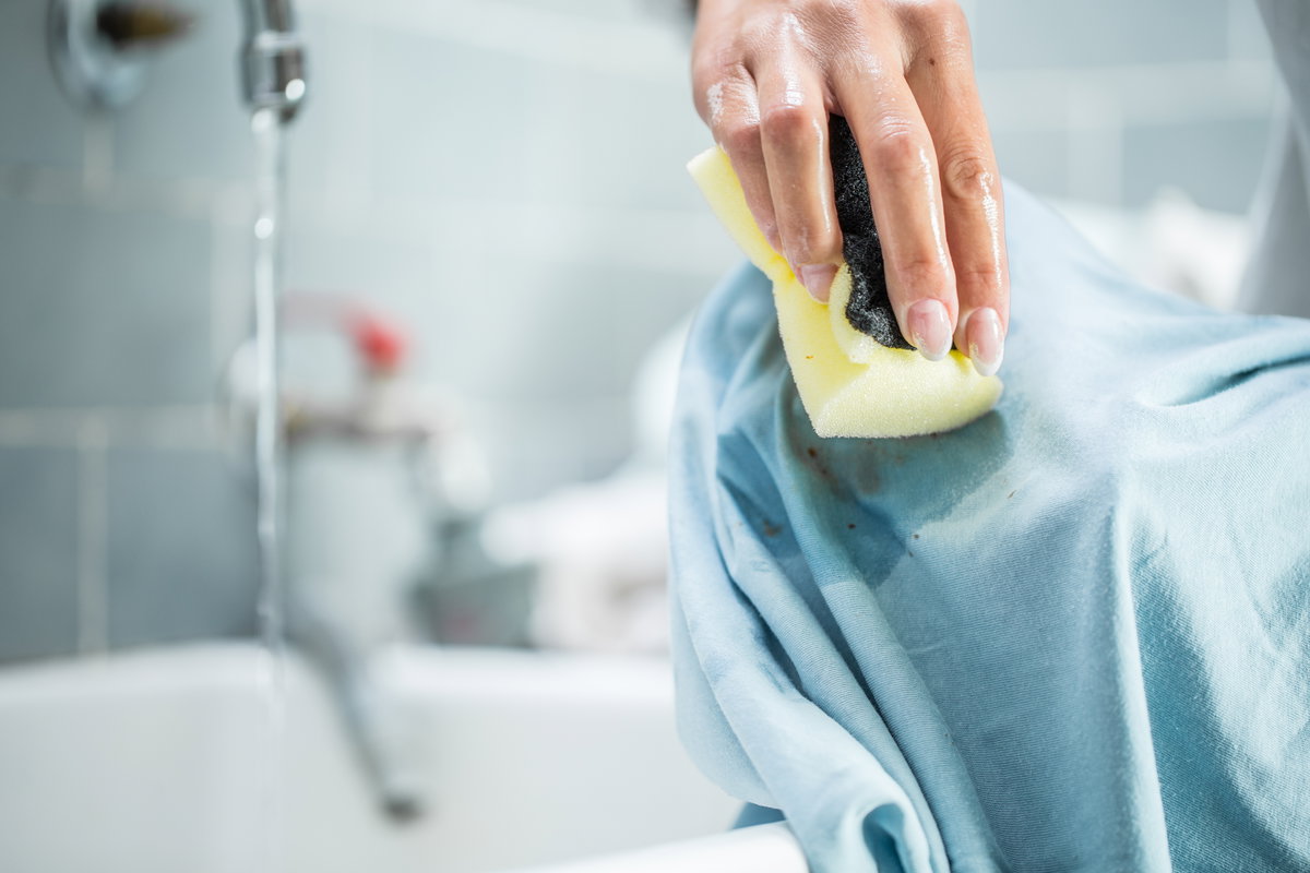 Fettflecken entfernen: Hand wäscht Fleck mit Schwamm aus Kleidungsstück