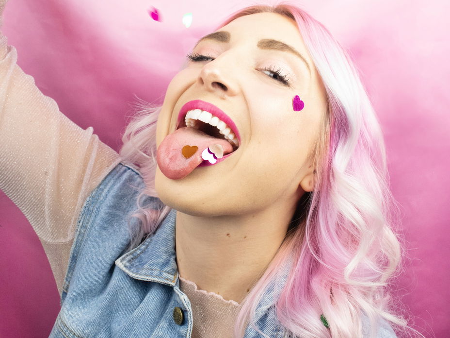 Horoskop: Frau mit rosa Haaren und Konfetti im Mund