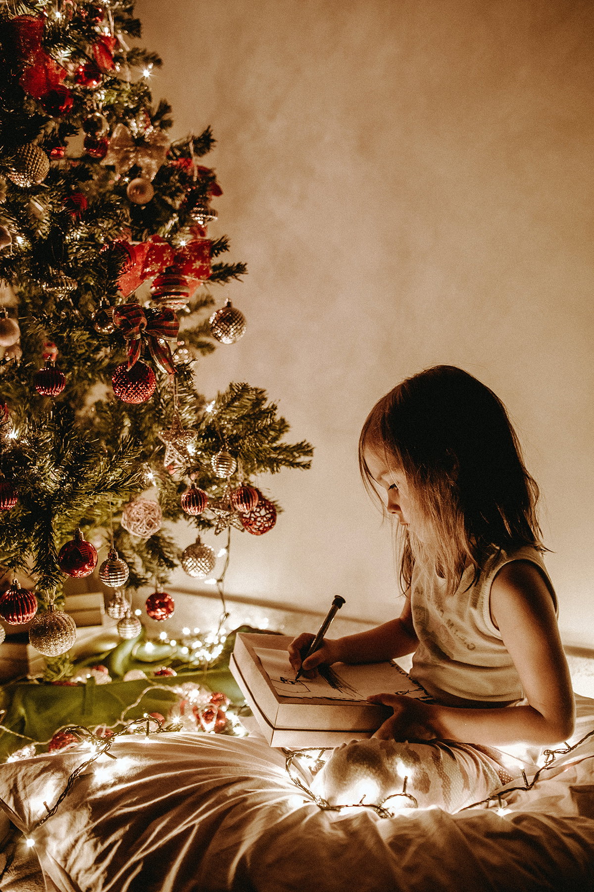 Kleines Mädchen malt vor dem Weihnachtsbaum