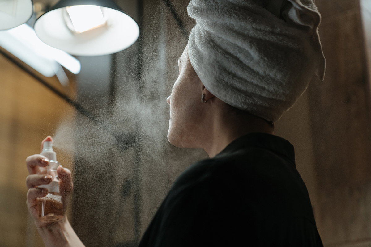 Frau sprüht Gesichtsspray auf ihr Gesicht