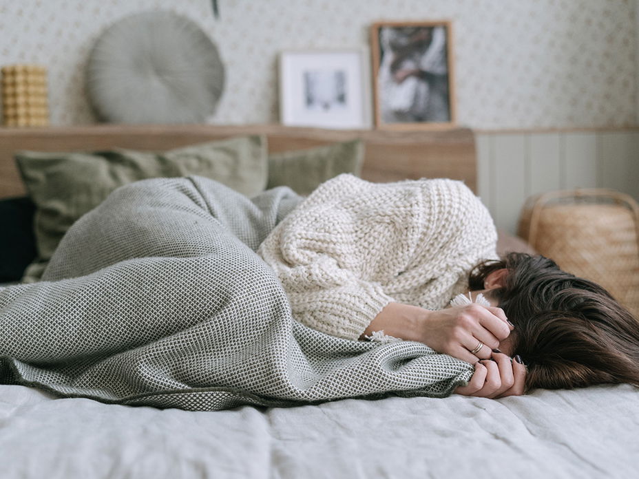 Frau im Bett mit Händen vor Gesicht