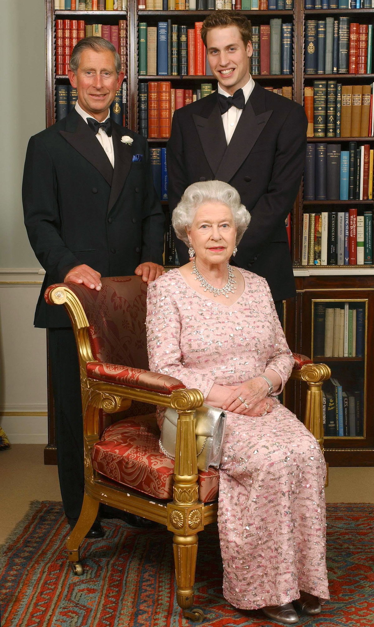 Queen sitzt auf einem Stuhl. Hinter ihr stehen Prinz Chalres und Prinz William