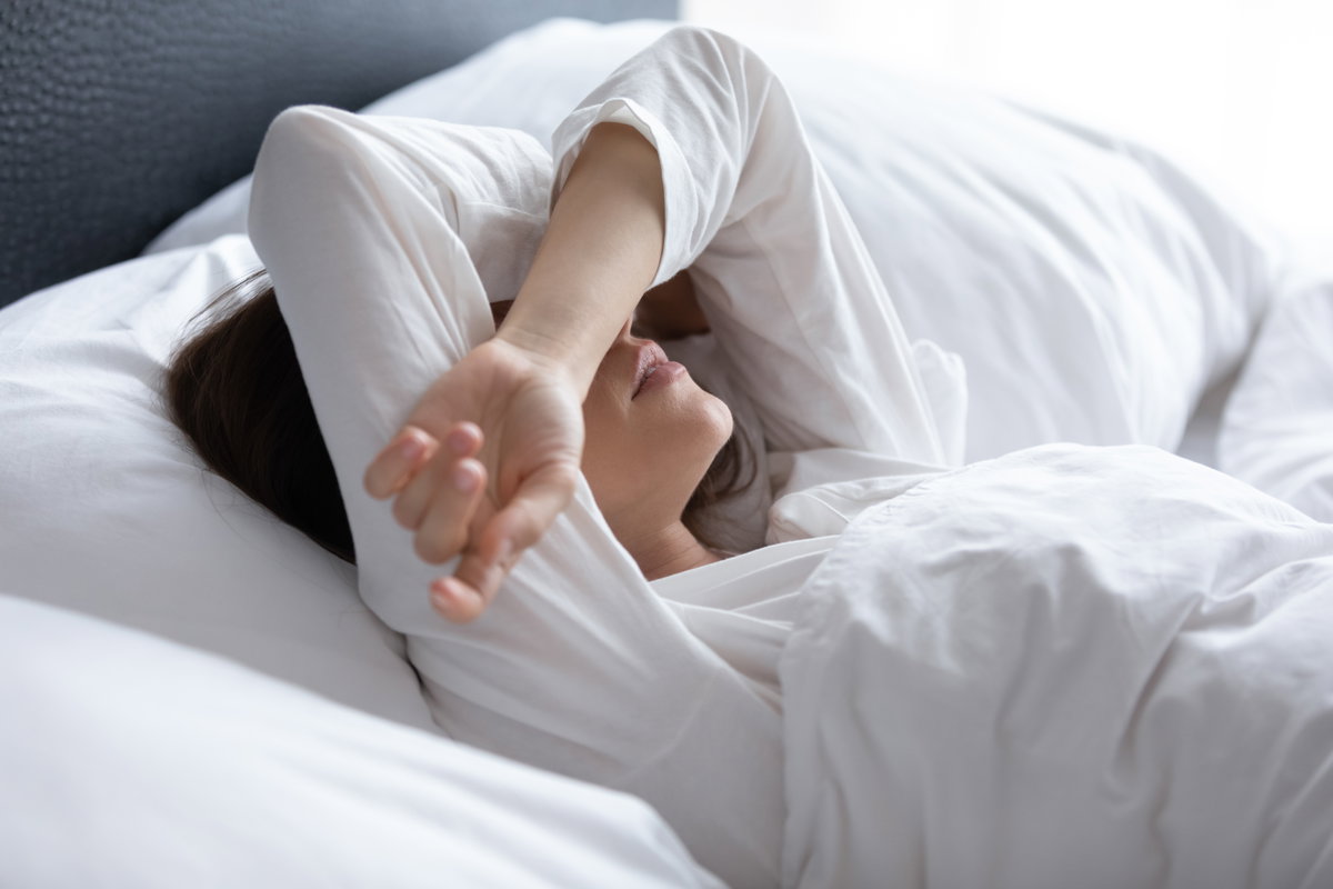 Frau rauft Arme über den Kopf zusammen und liegt im Bett