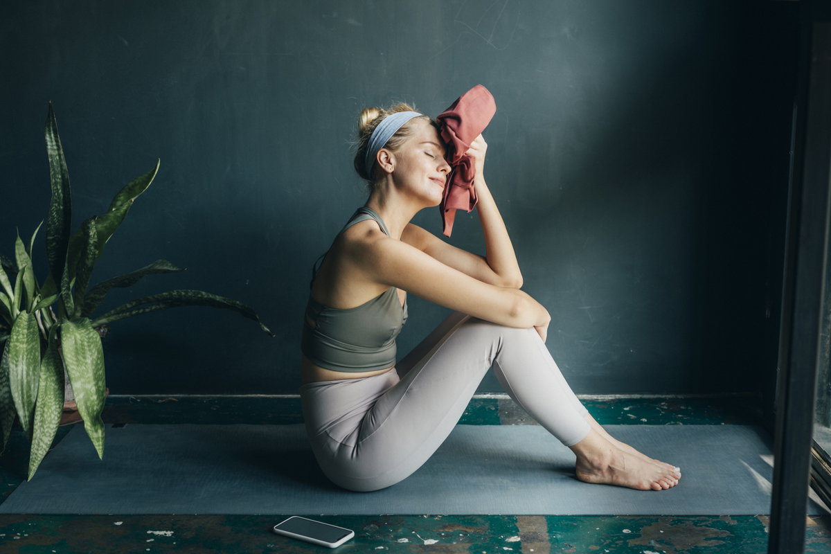 FGrau sitzt auf Yogamatte und hält sich ein Handtuch an den Kopf