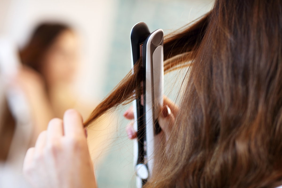 Frau glättet sich die Haare mit Dampfglätteisen