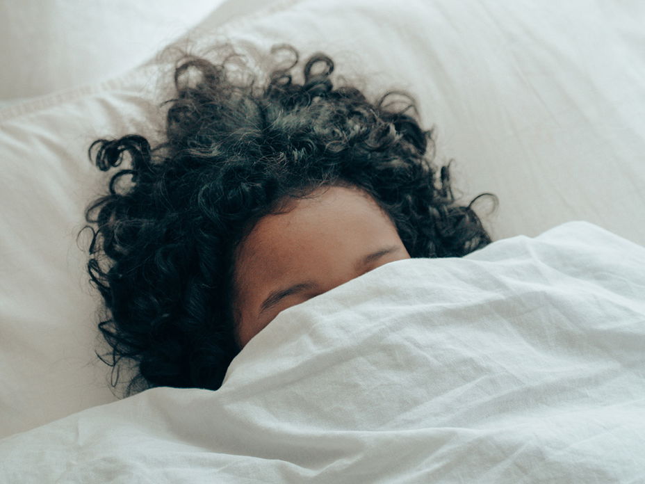Frau im Bett mit Decke über dem Kopf