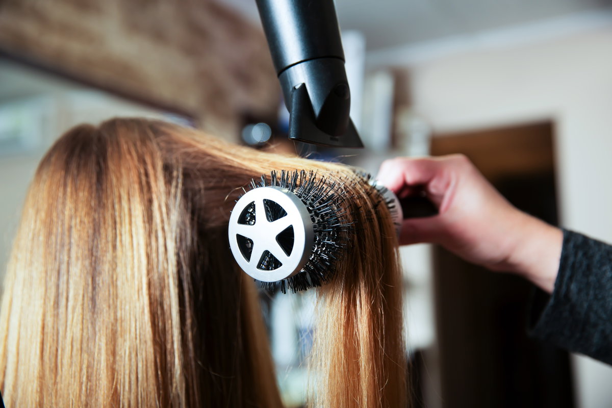 Frau werden die Haare auf einer Rundbürste geföhnt