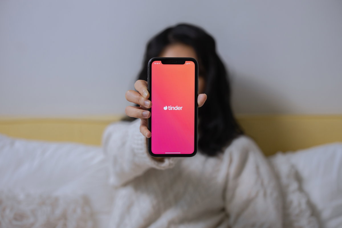 Frau hält Handy mit geöffneter Tinder-App hoch