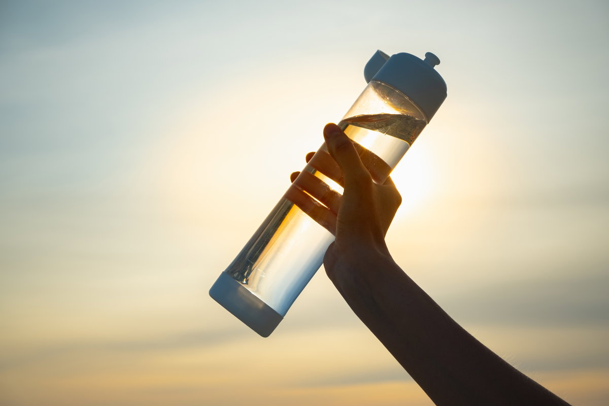 Frau hält Trinkflasche in die abendliche Sonne