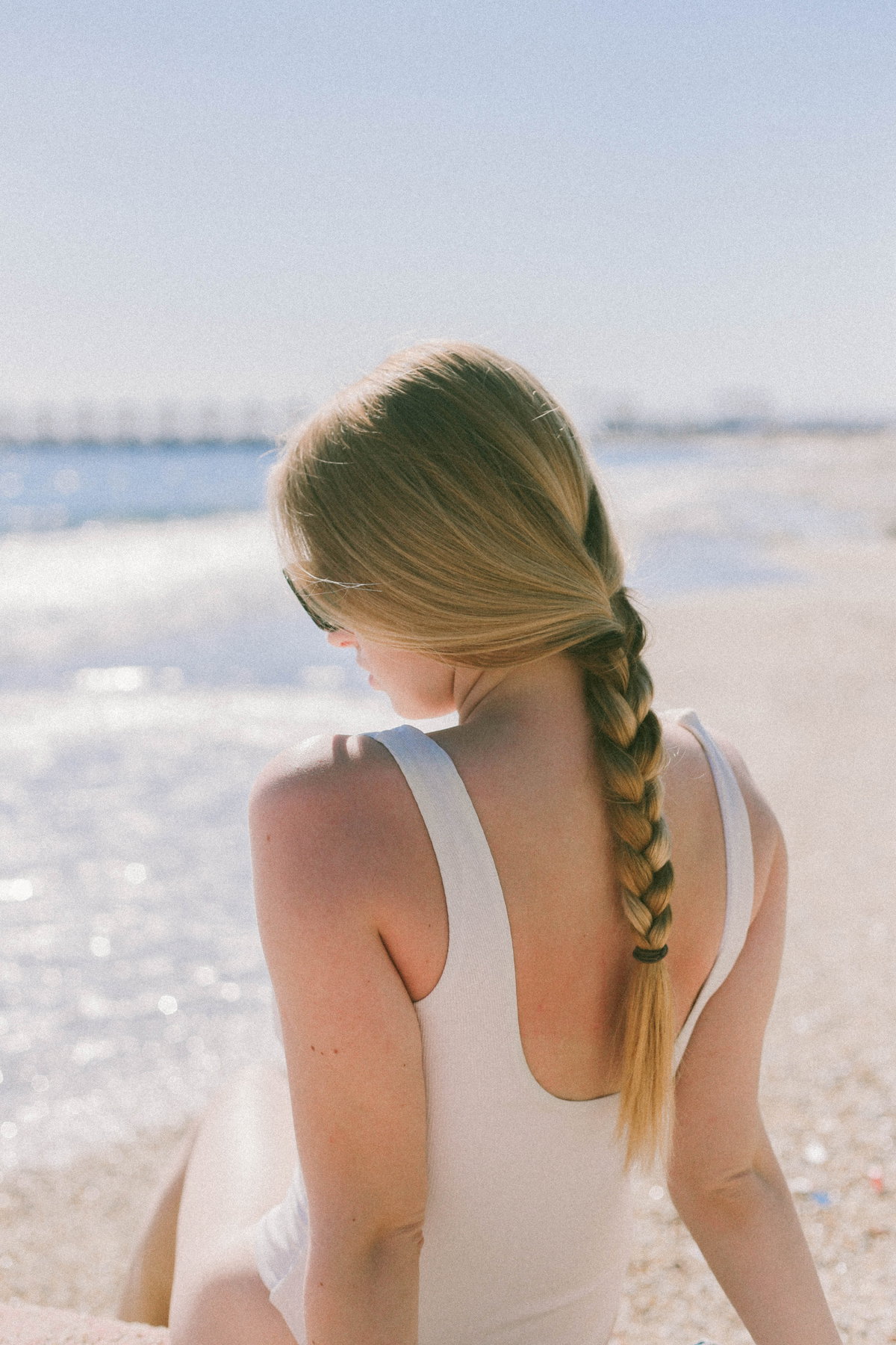 Frau mit geflochtenen Haaren sitzt am Strand