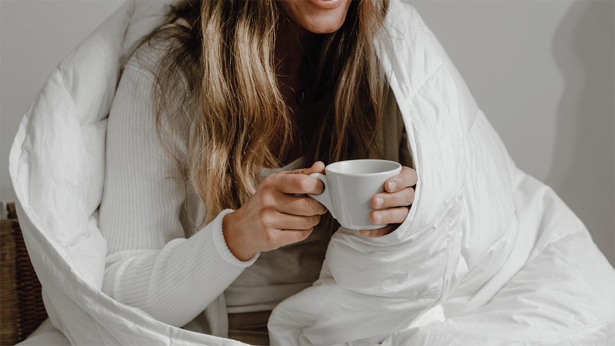 Frau mit Tasse im Bett mit Decke