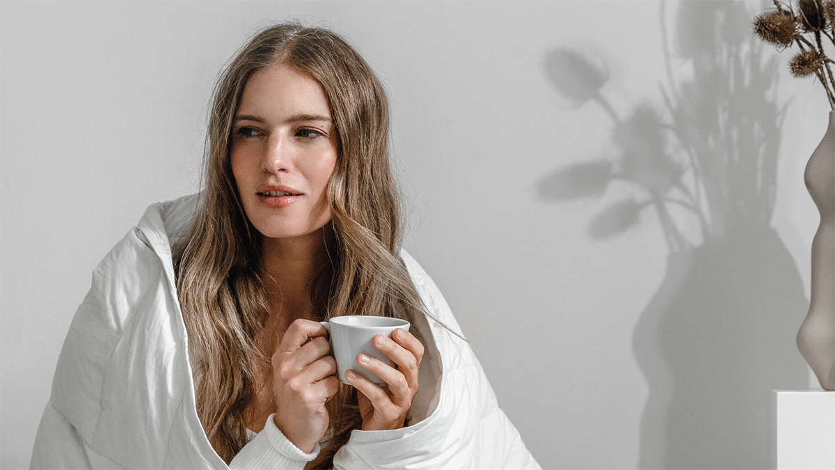 Frau hält Tasse in der Hand und trägt eine Decke