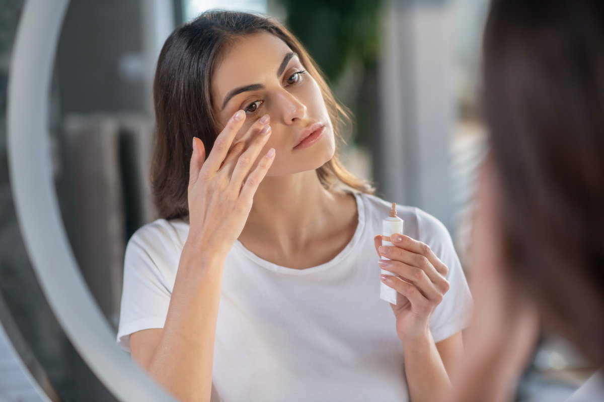 Frau deckt Augenringe mit Concealer ab