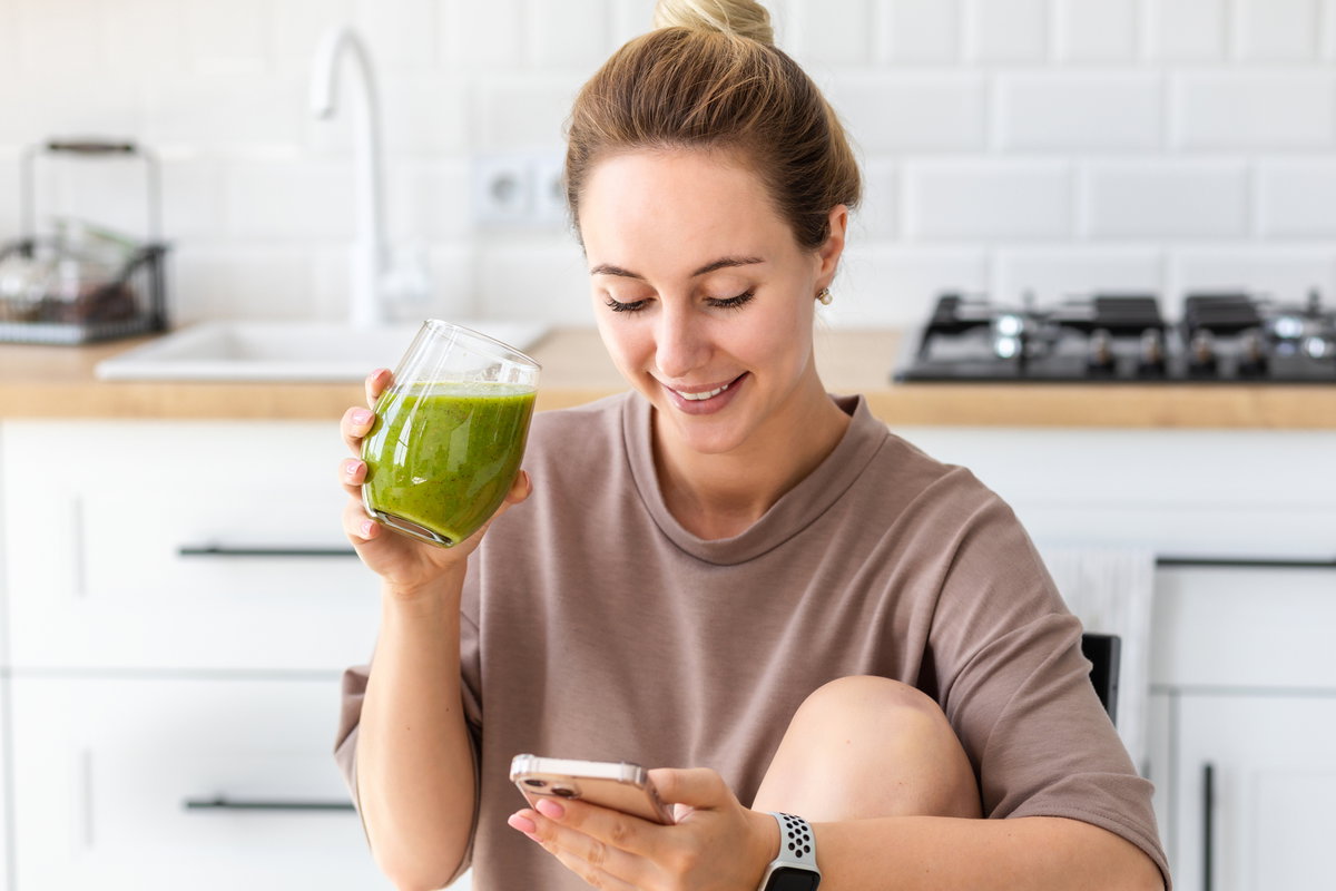 Frau mit grünem Saft schaut auf Handy