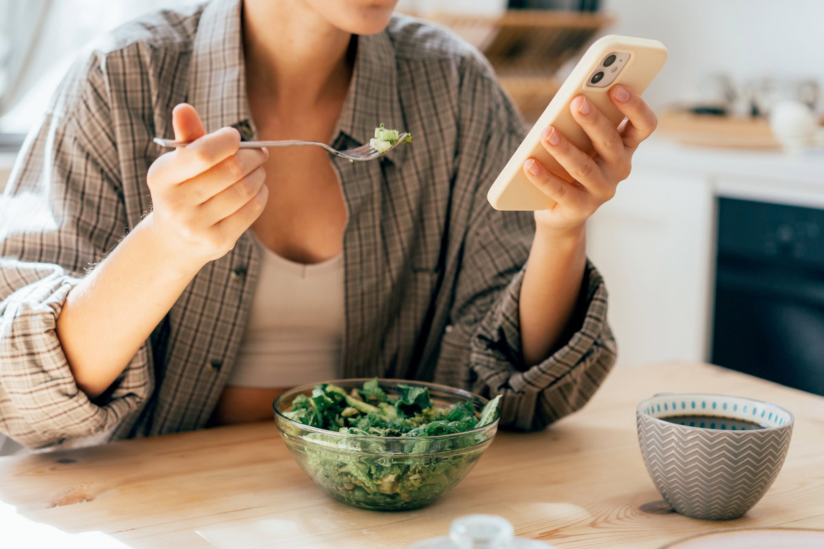Frau isst Salat mit Smartphone in der Hand