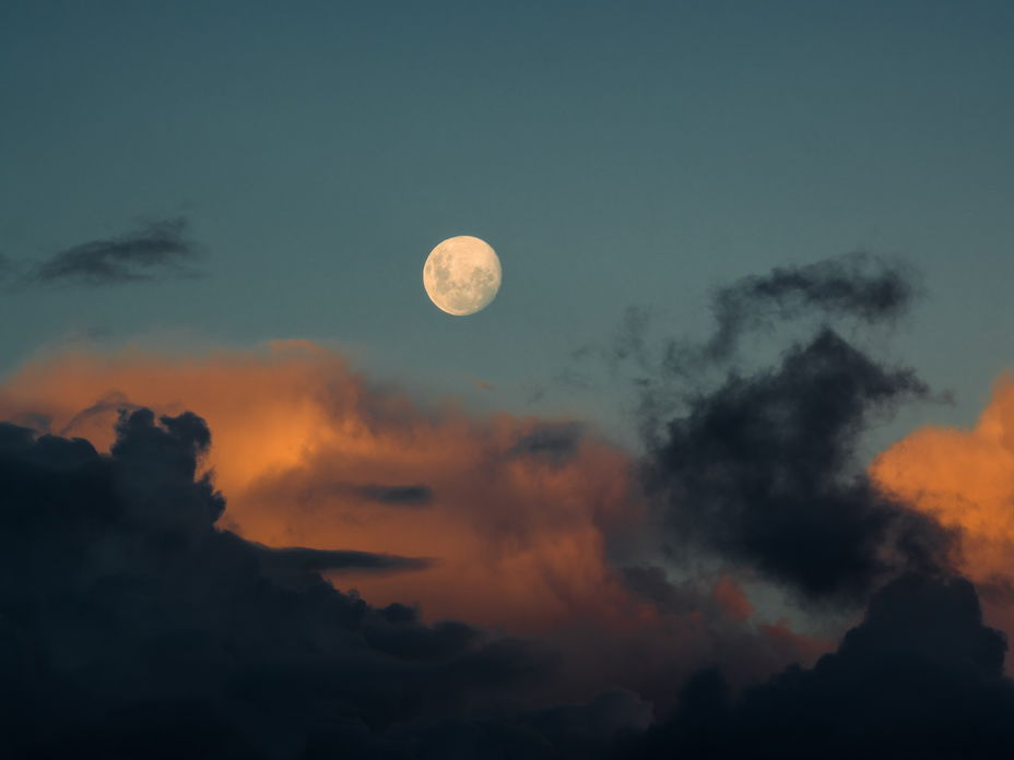 Vollmond am blauen Himmel mit orangefarbenen Wolken