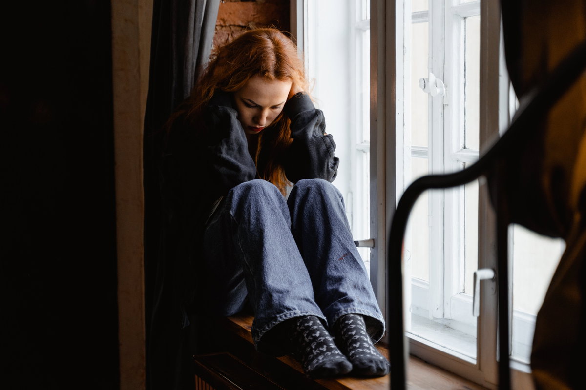 Traurige Frau sitzt auf einer Fensterbank
