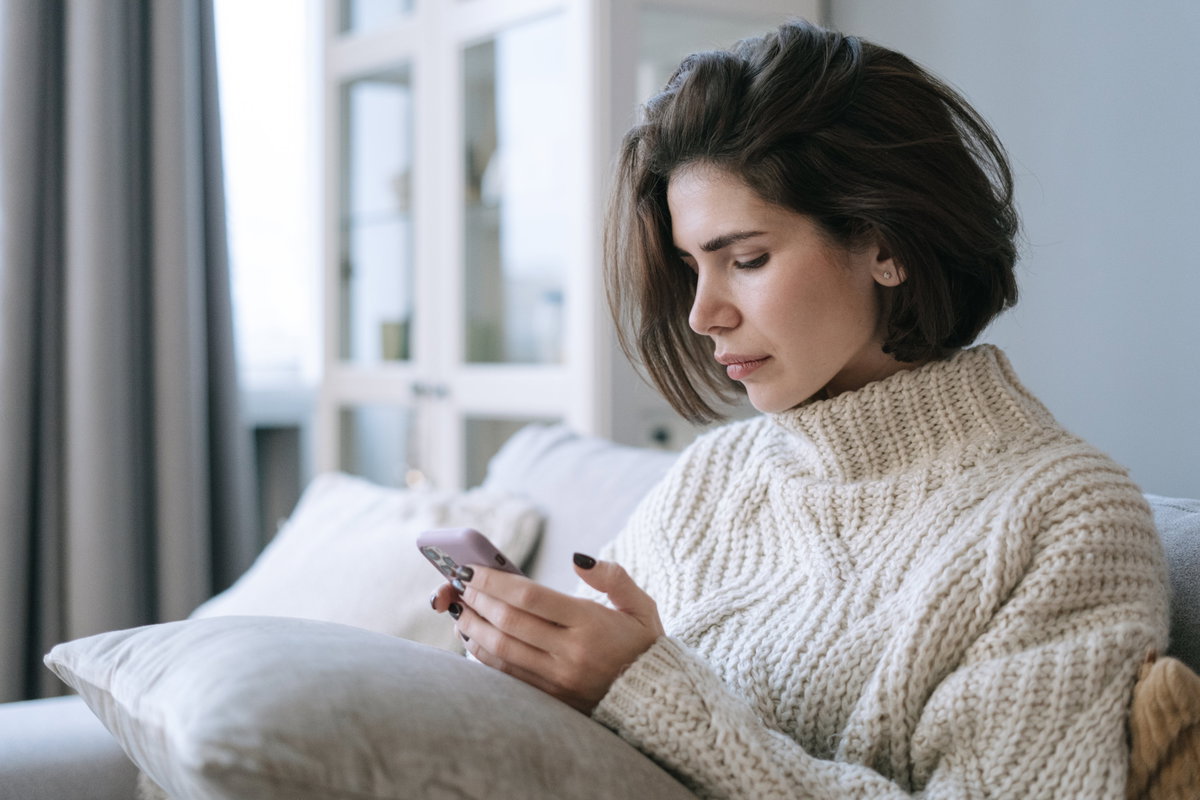 Frau mit kurzen braunen Haaren schaut traurig auf ihr Smartphone