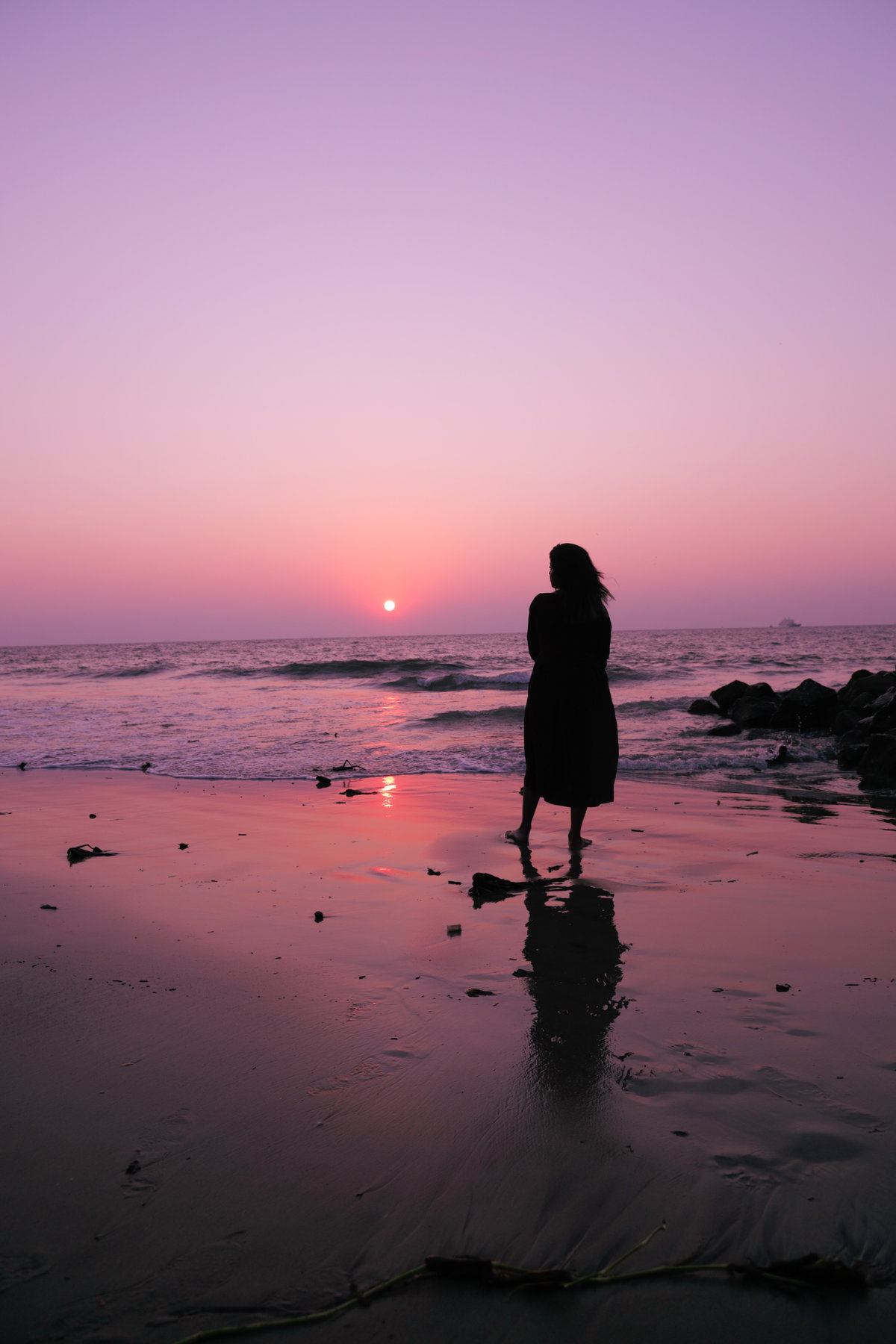 Frau steht am Strand und schaut den Himmel an