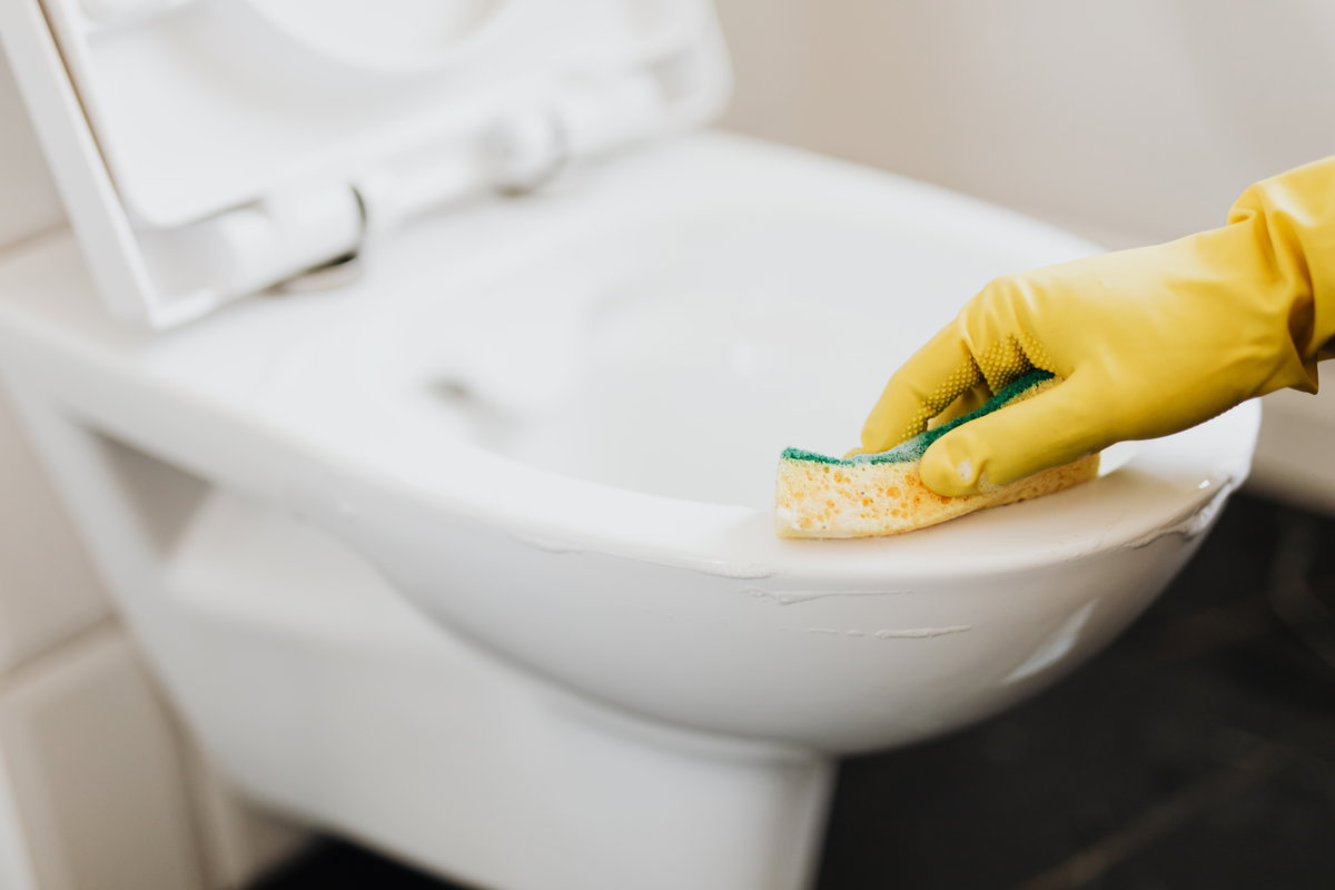 Person putzt eine weiße Toilette mit einem gelben Schwamm