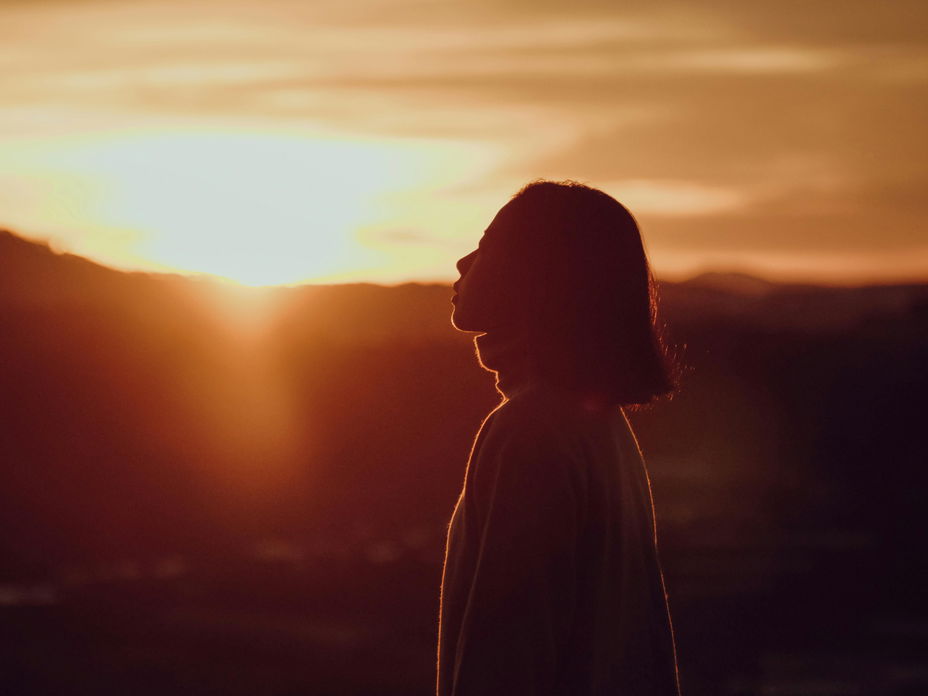 Frau mit kurzen Haaren steht vor einem Sonnenuntergang