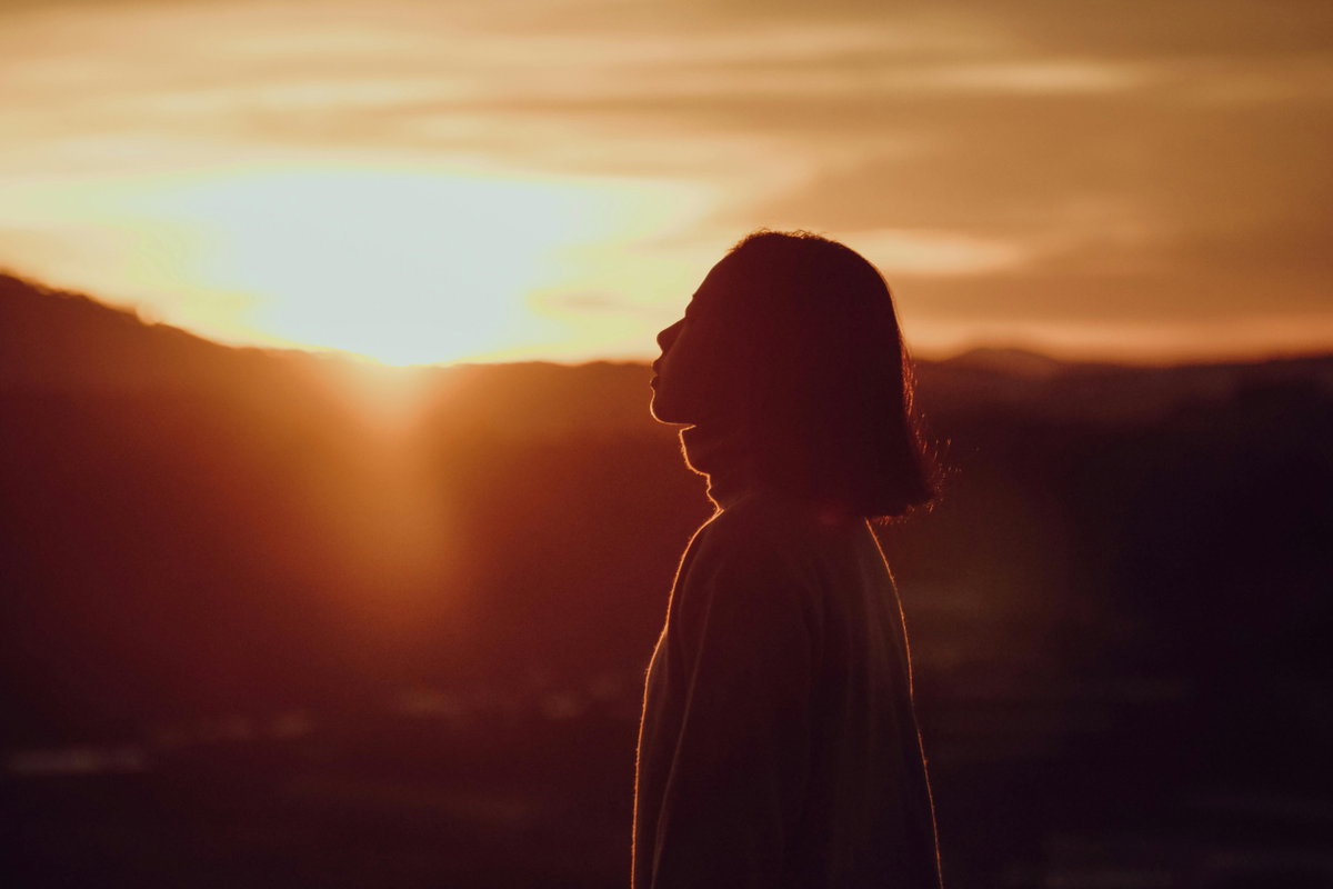 Frau mit kurzen Haaren steht vor einem Sonnenuntergang