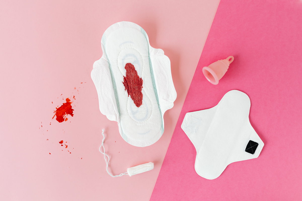 Binden, Tampon und Menstruationstasse liegen auf einem rosafarbenen Hintergrund
