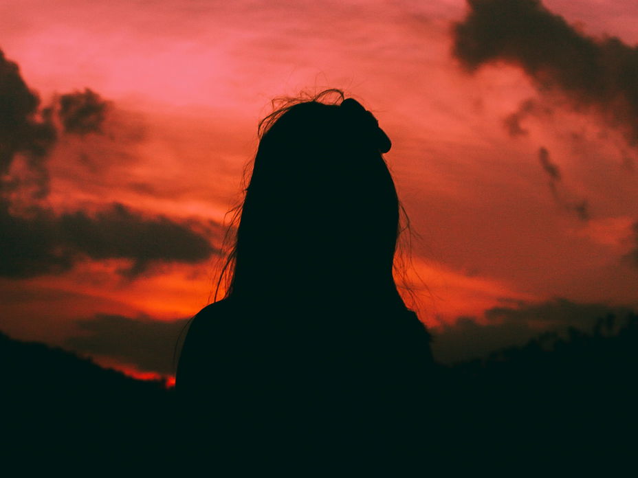 Silhouette einer Frau mit langen Haaren vor einem orange-rosafarbenen Himmel