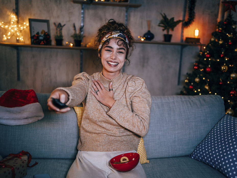 Frau sitzt auf dem Sofa und guckt in ihrer weihnachtlich dekorierten Wohnung Fernsehen