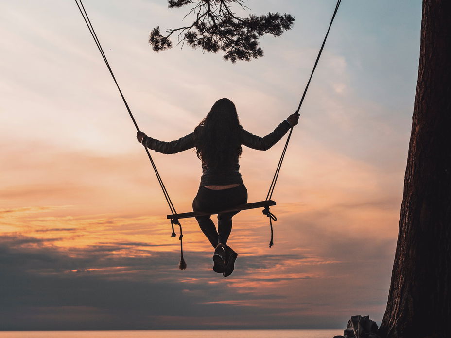 Frau auf einer Schaukel beim Sonnenaufgang