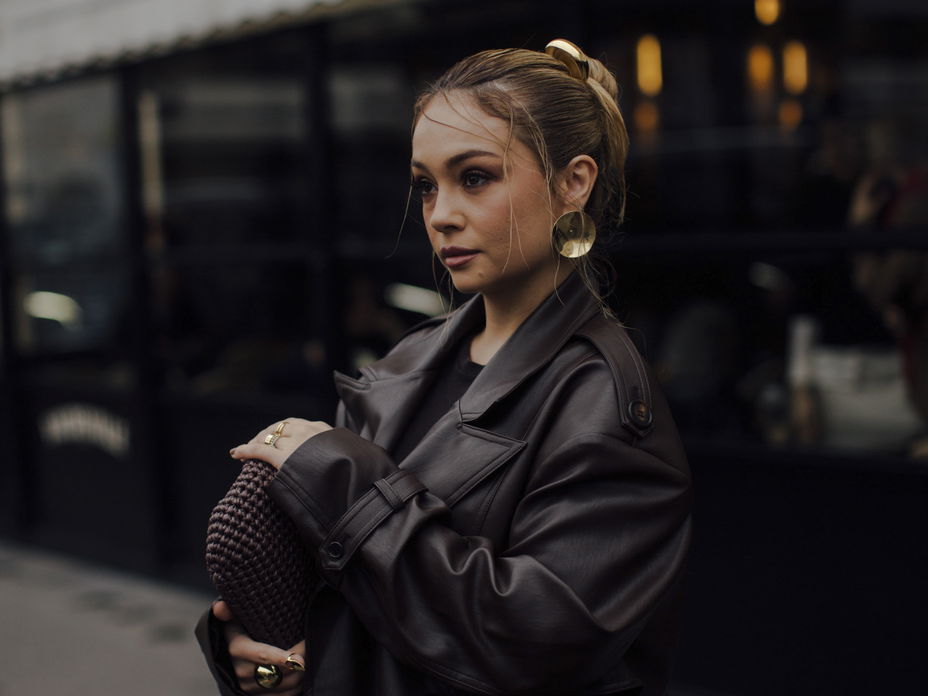 Frau trägt auf Paris Fashion Week braunen Ledermantel goldene Ohrringe und braune Tasche
