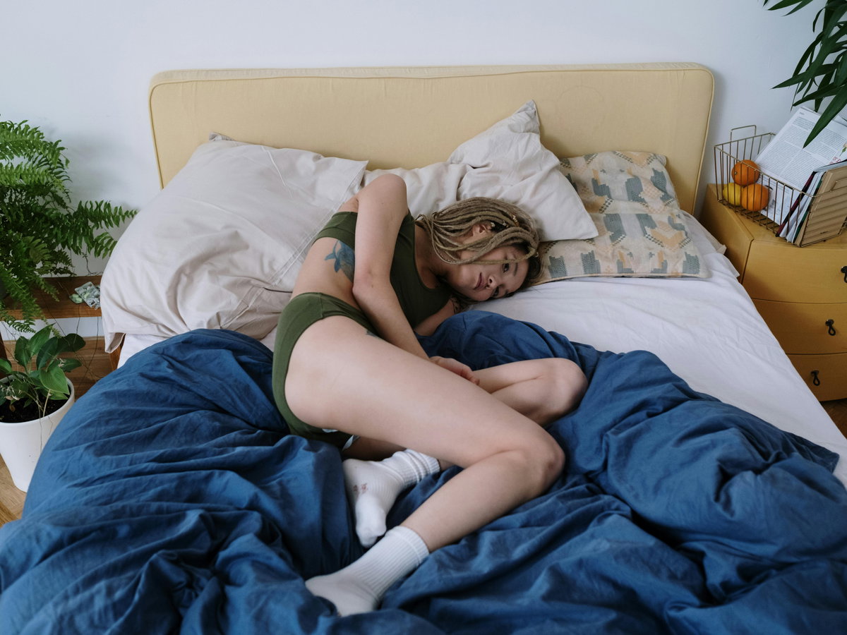 Frau liegt mit Schmerzen im Bett