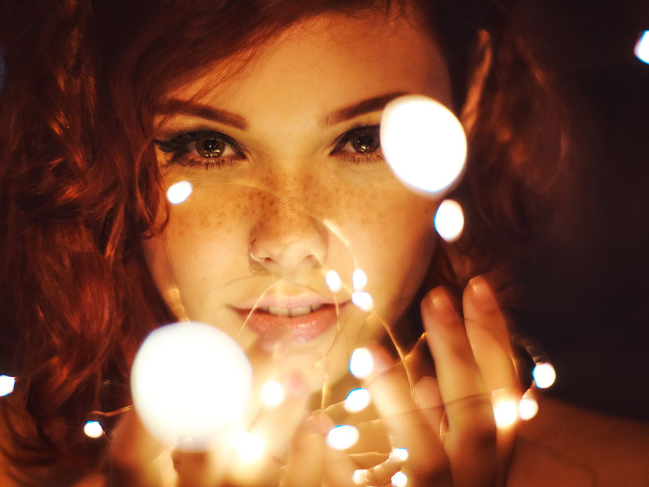 Frau mit Sommersprossen und Eyeliner hält eine Lichterkette in der Hand
