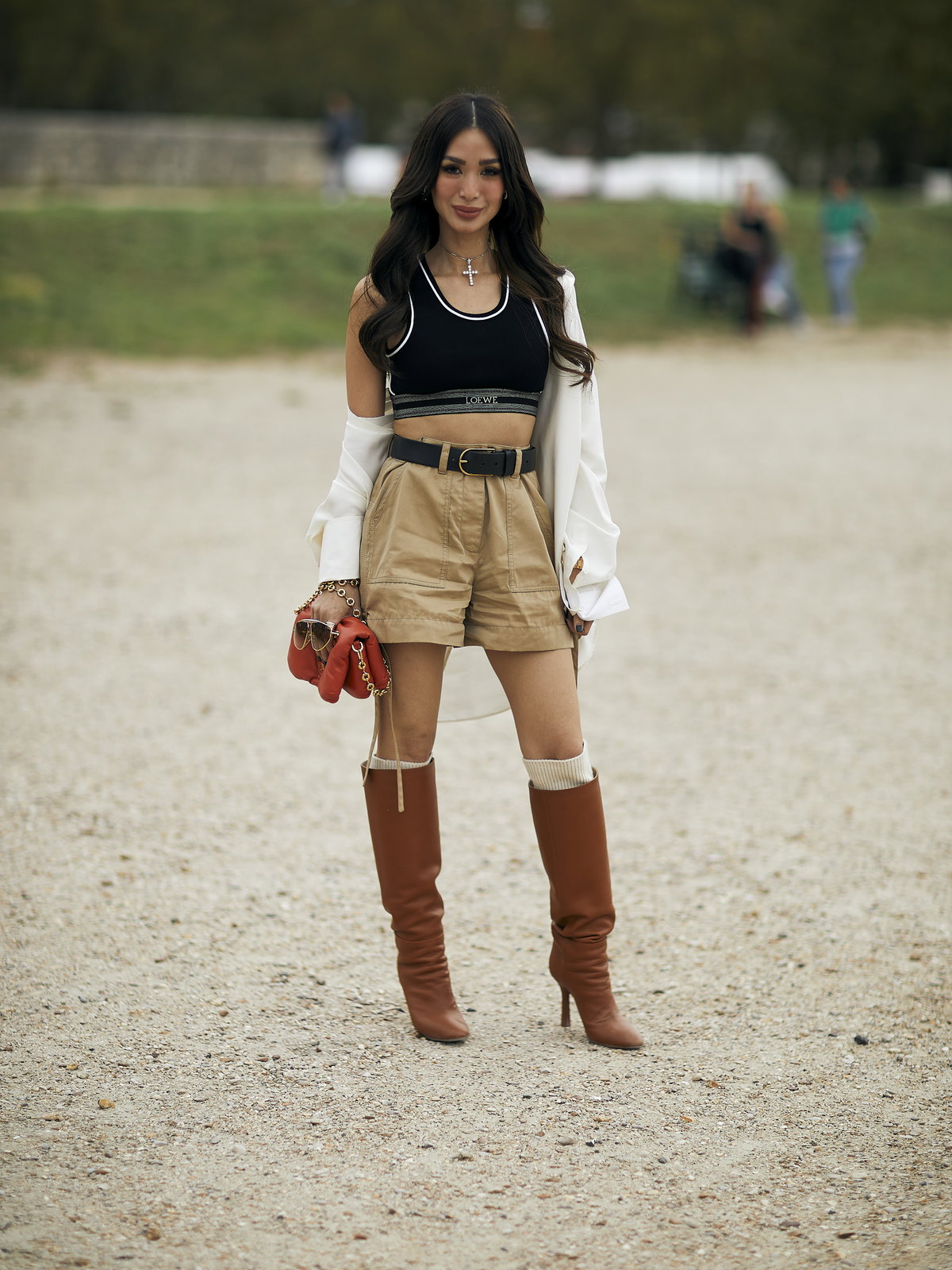 Frau trägt auf Paris Fashion Week beigefarbene Shorts mit weißem Hemd und Sport-BH sowie kniehohe Stiefel